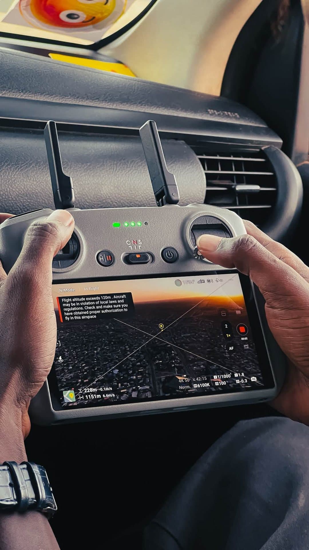 Drone controller showing a live aerial view at sunset, held inside a car